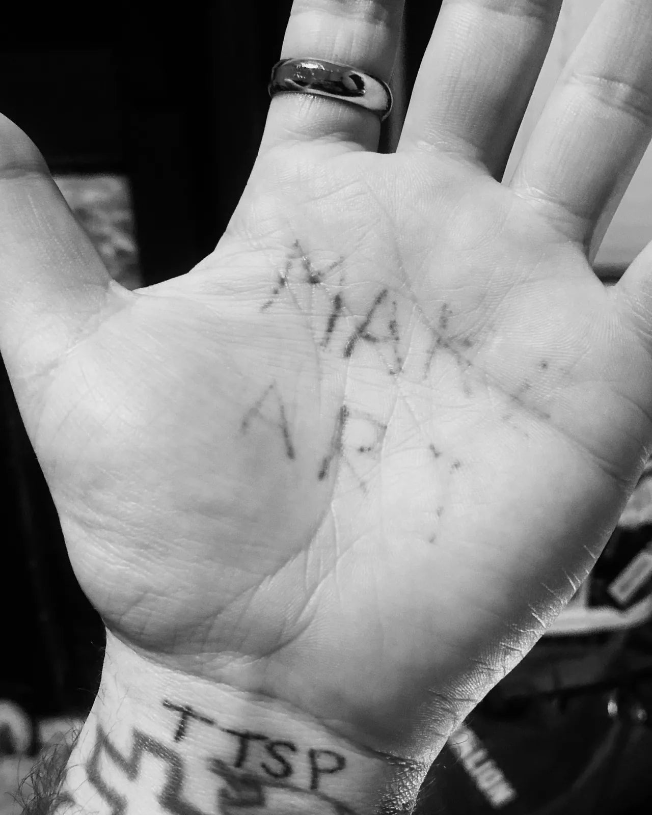Black-and-white photo of an open palm with the words MAKE ART tattooed across it